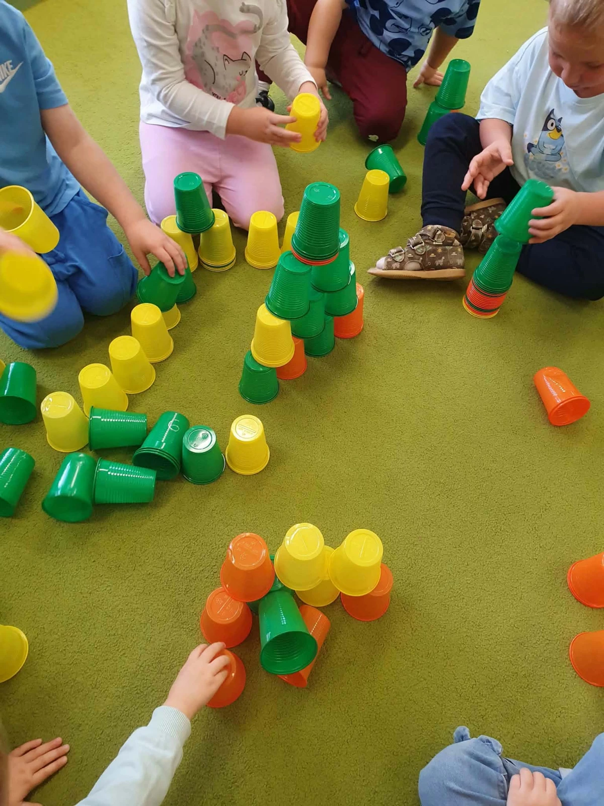 Dzieci układają kolorowe plastikowe kubeczki w wieże na dywanie.