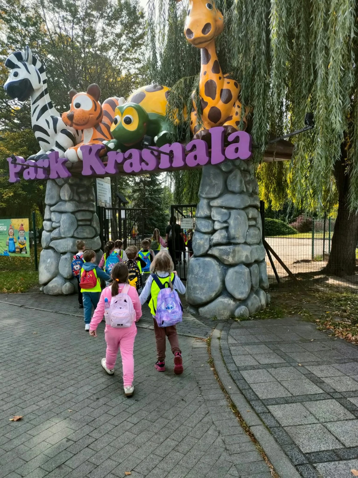 Grupa dzieci wchodzi przez bramę Parku Krasnala w Nowej Soli.